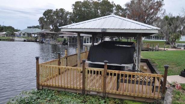 A covered outdoor grill area with a wooden deck and a view of the water.