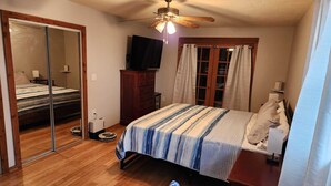 A bedroom with a bed, a ceiling fan, a TV, a wardrobe, and a sliding door.