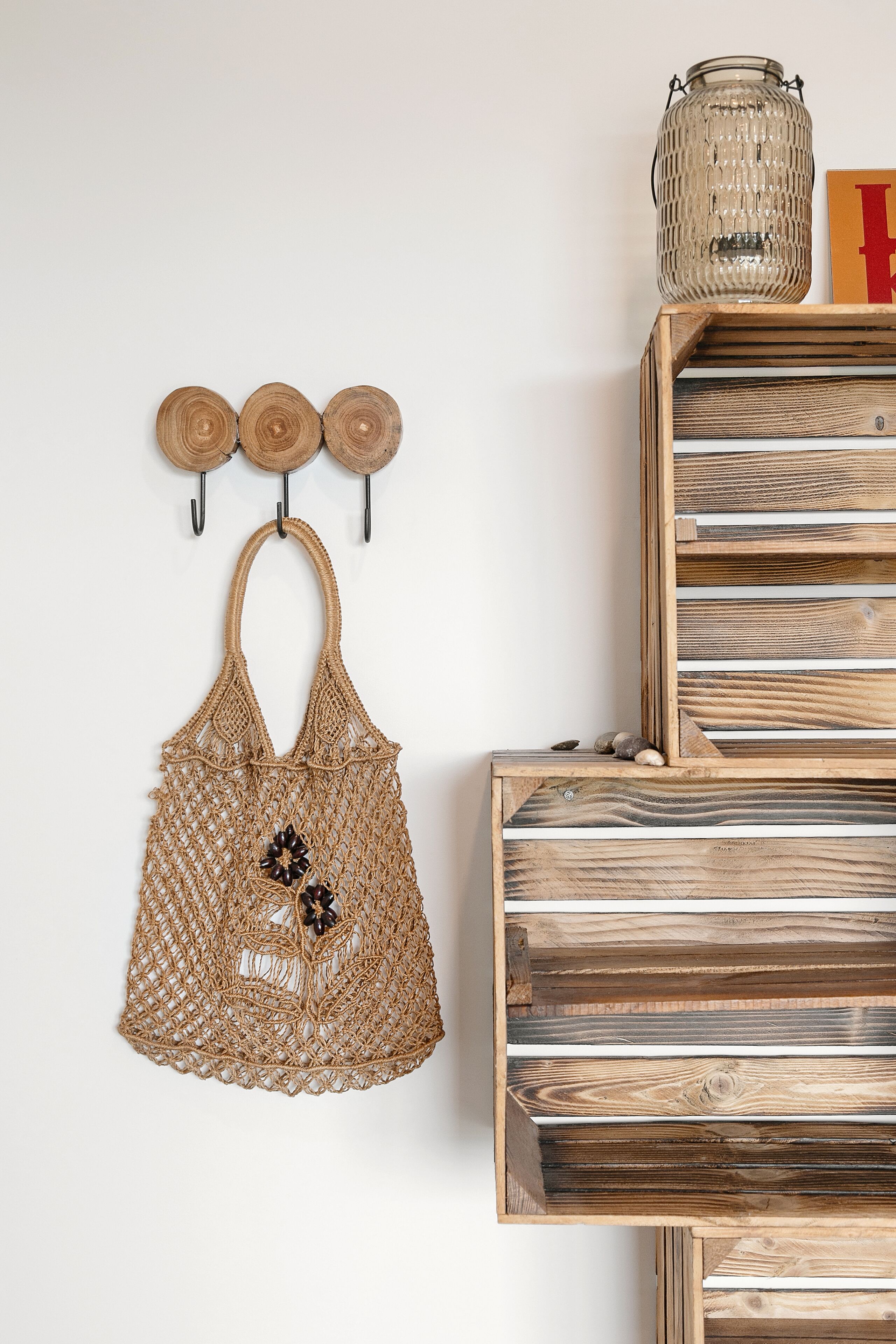 A wall-mounted macrame bag with a decorative flower, a wooden shelf with a glass jar, and a wooden slat wall panel.