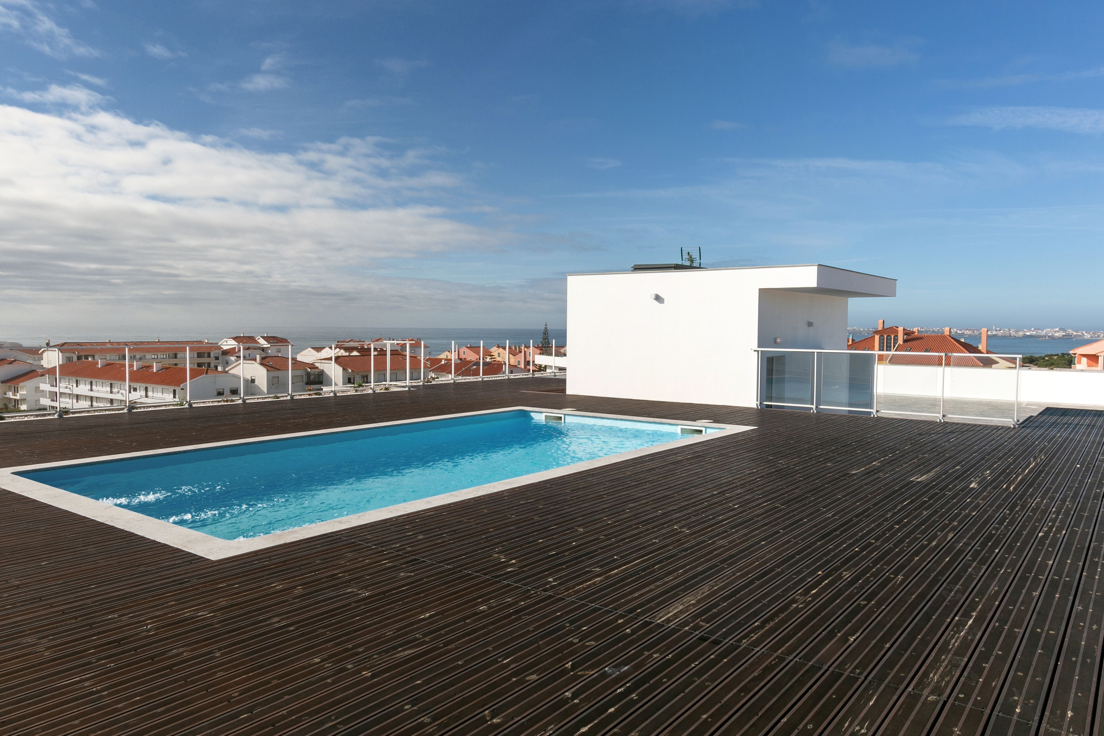 Una piscina sul tetto con un pontile di legno, circondata da edifici con tetti rossi, sotto un cielo sereno.