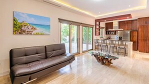 Een moderne woonkamer met een leren bank, een glazen salontafel en een keuken met houten kastjes en een roestvrijstalen koelkast.