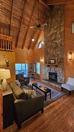 A cozy log cabin interior with a stone fireplace, wooden ceiling beams, and a comfortable seating area. - Southern Oak-Best views of the Mountains (Blairsville)
