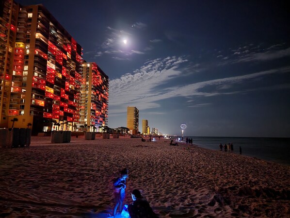 A beachside hotel with multiple balconies, a sandy beach, and a view of the ocean.
