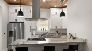 Una cucina moderna con mobili bianchi, un frigorifero in acciaio inossidabile, un'isola in marmo con sgabelli da bar e illuminazione a sospensione.