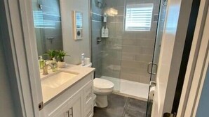 A modern bathroom with a glass shower enclosure, a white sink with a mirror, and a toilet. - Modern Studio Apartment in Central West end, BJ Hospital (St. Louis)