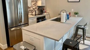 A modern kitchen with stainless steel appliances, a white countertop, and a small island with stools. - Modern Studio Apartment in Central West end, BJ Hospital (St. Louis)