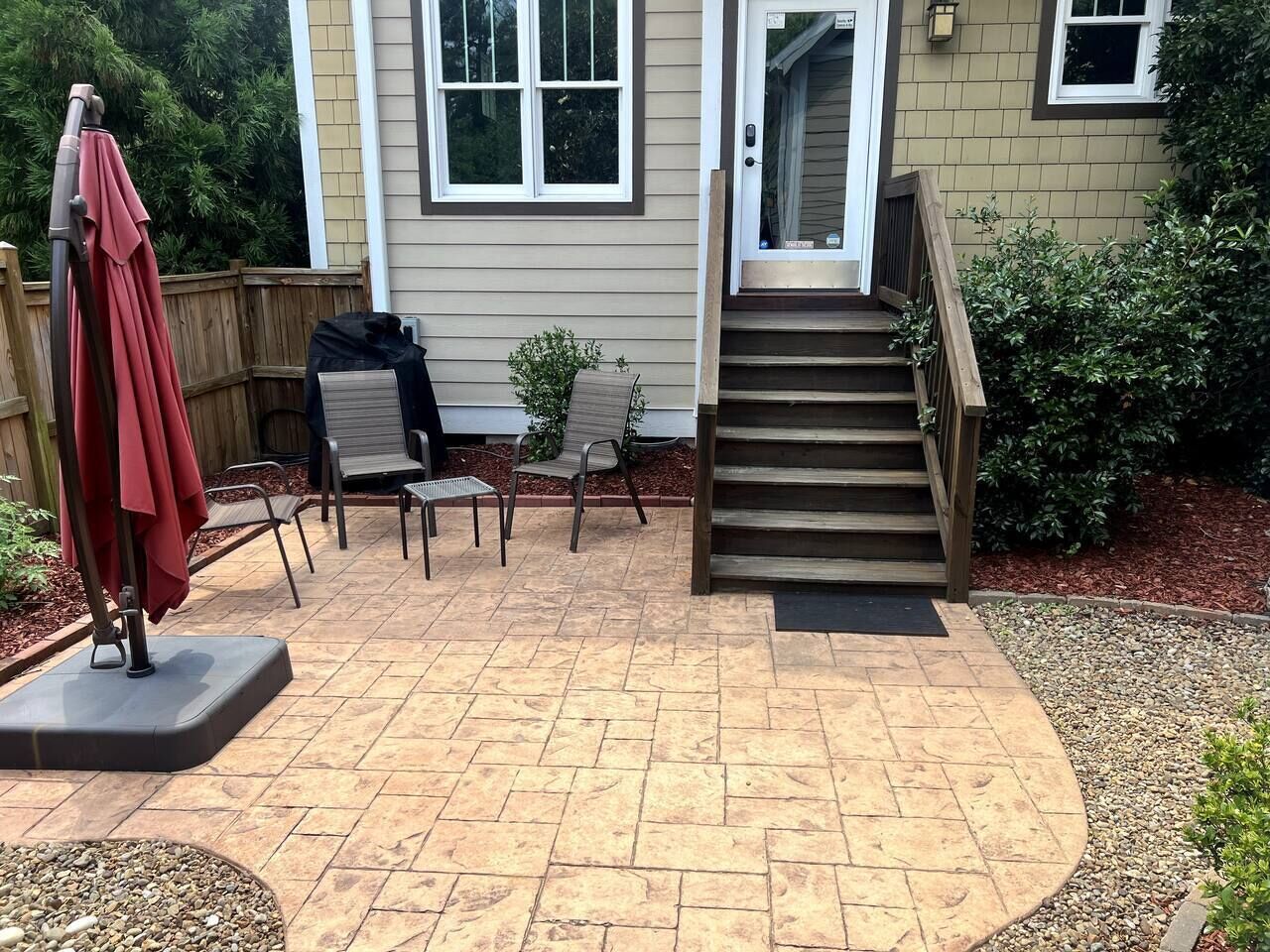 Un patio con mobiliario exterior, una escalera de madera y una casa al fondo.