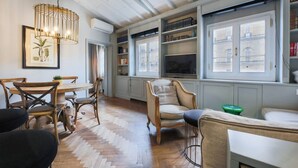 A room with a herringbone floor, a wooden dining table with chairs, a sofa, a chair, a hanging light fixture, and a bookshelf with books. - Apartments Florence- Pitti 8 with amazing view (Firenze)