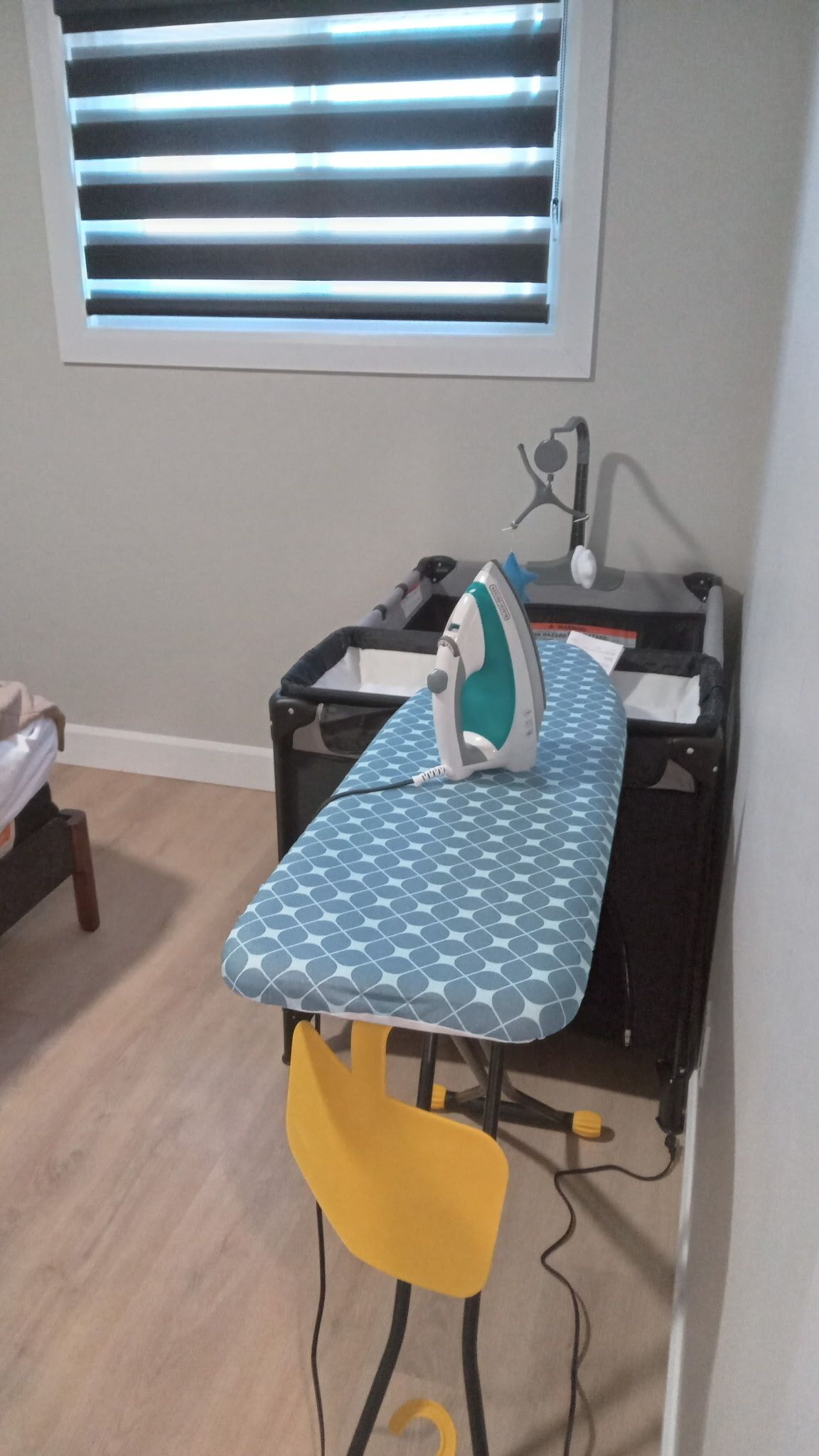 Estación de planchado compacta con tabla de planchar estampada, un planchador y una silla amarilla.