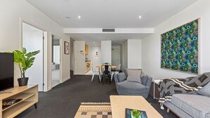 Un salon moderne doté d’un téléviseur à écran plat, d’une table basse, d’un canapé gris et d’un coin repas avec une table et des chaises.