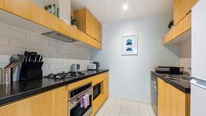Une cuisine compacte avec des meubles de rangement en bois, une cuisinière à gaz, un four à micro-ondes et un lave-vaisselle.