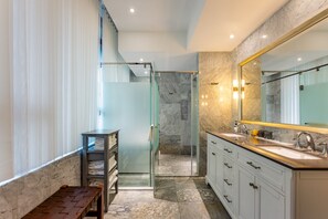 A modern bathroom with a glass shower enclosure, marble flooring, and a large mirror.