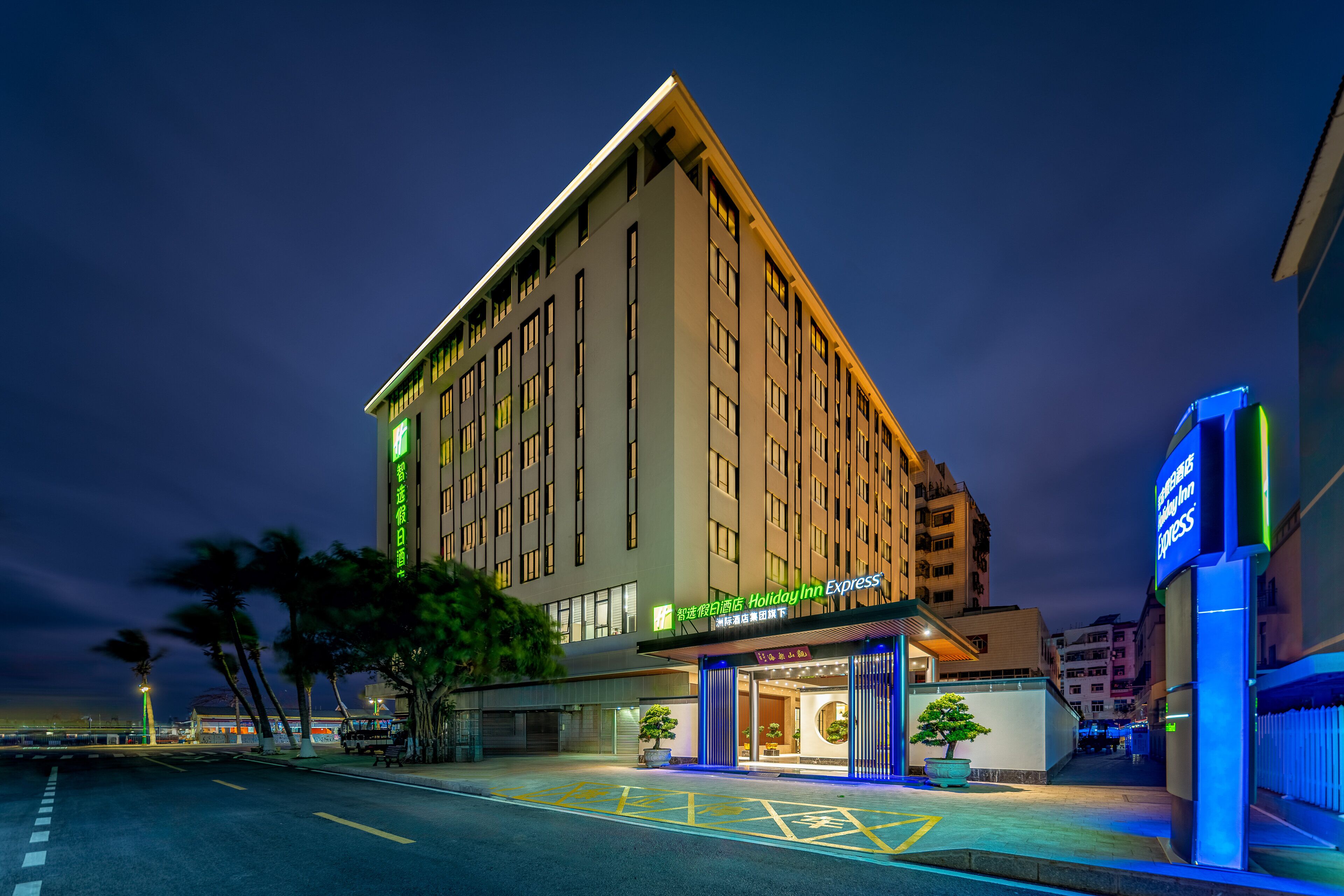 A multi-story hotel with a prominent entrance, a parking lot, and a well-lit facade.