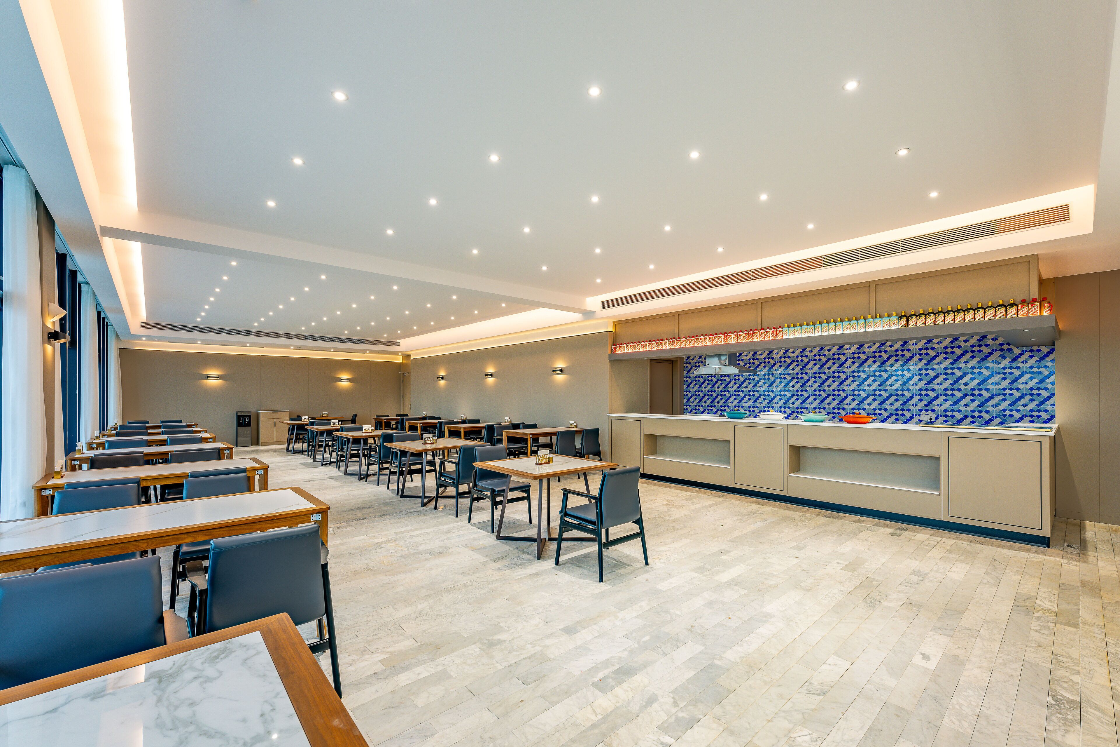 Un espace repas moderne avec des tables et des chaises, un comptoir de cuisine avec des bouteilles et un mur décoratif à motifs.