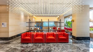 Un hall d’entrée agrémenté d’un lustre moderne, de sièges en cuir rouge et d’un comptoir d’accueil.