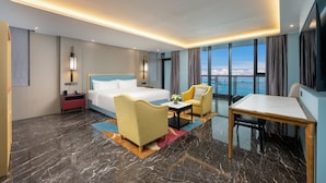 Une chambre d’hôtel avec un lit, un bureau, une chaise, une table de chevet et une vue sur la mer.