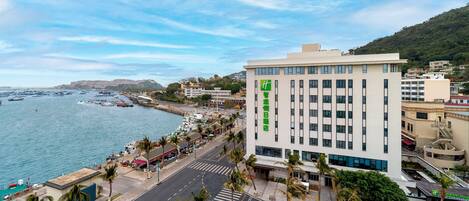 A hotel with a view of the sea, located near a busy street with a pedestrian crossing.