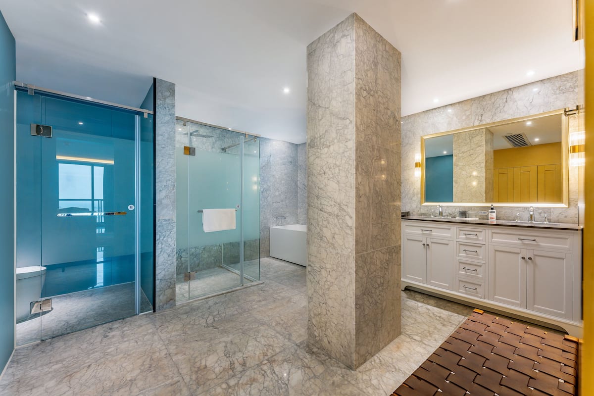 A modern bathroom with a glass shower enclosure, a marble column, and a large mirror above the sink.
