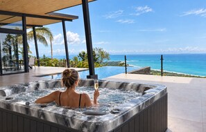 Una mujer relajándose en un jacuzzi con vista al océano y palmeras.