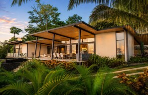 A modern house with a covered patio, large windows, and lush greenery.