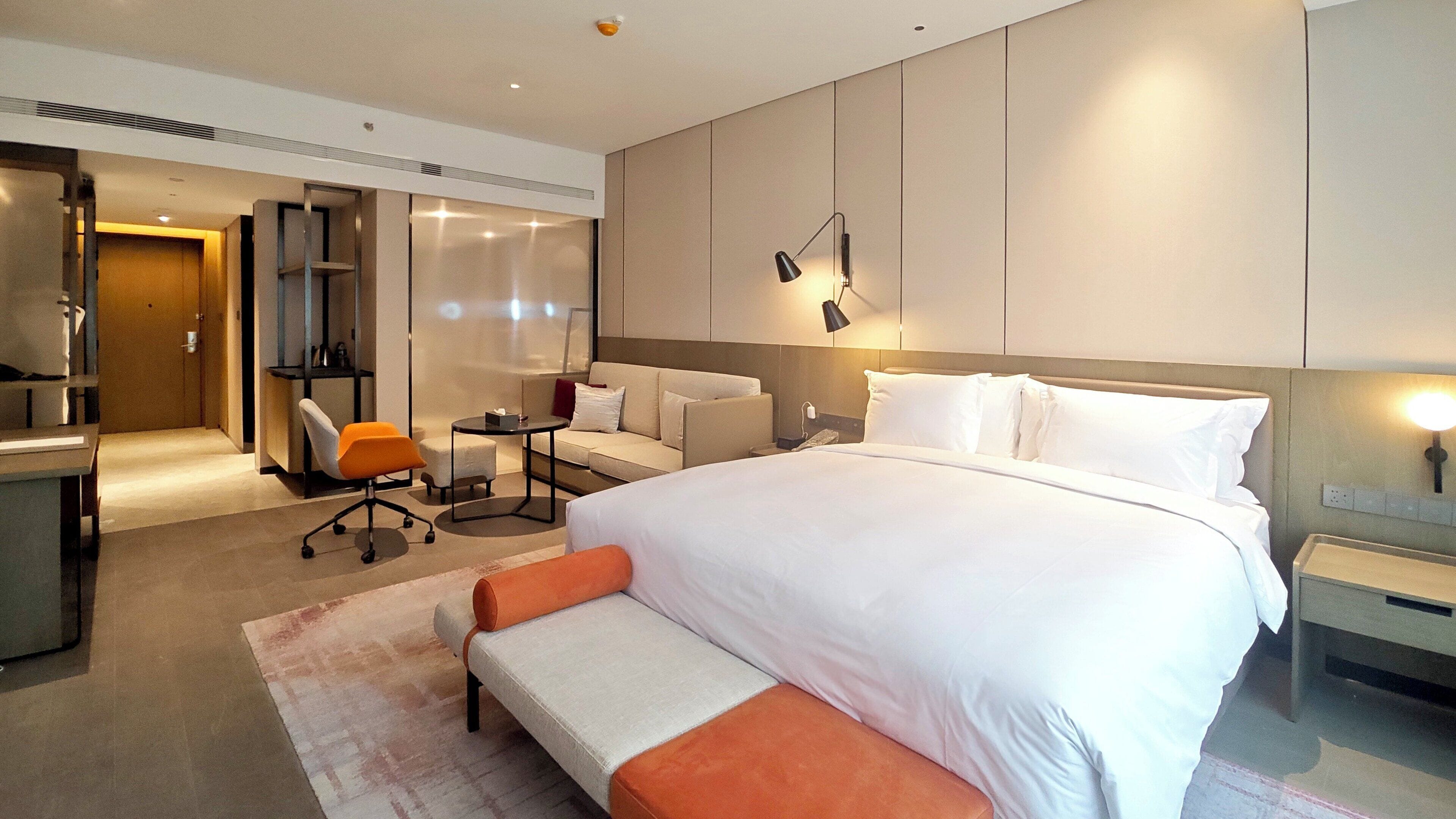 Quarto de hotel com uma cama grande, uma escrivaninha, uma cadeira, uma mesinha e um sofá.