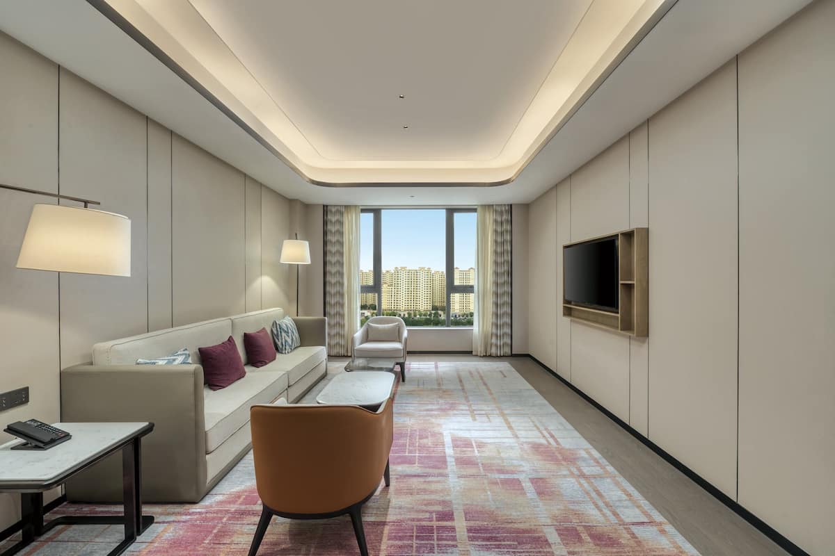 Une chambre d’hôtel moderne, dotée d’un canapé, d’un fauteuil, d’une télévision et offrant une vue sur la ville grâce à de grandes fenêtres.