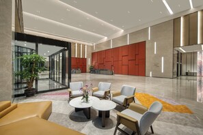 Un hall d’entrée moderne avec des espaces aménagés pour s’asseoir, un comptoir d’accueil et une grande plante.