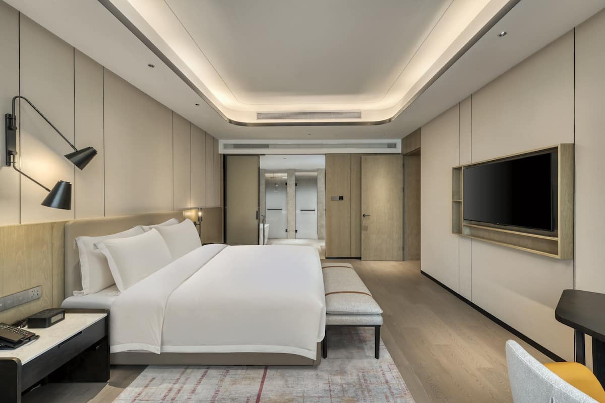 Une chambre d’hôtel moderne avec un grand lit, des tables de chevet, un téléviseur fixé au mur et un banc.