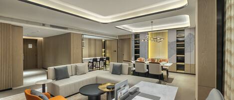A modern hotel lobby with a sectional sofa, a round coffee table, and a dining area with chairs and a table.