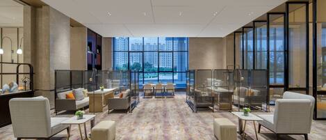 A spacious lobby with a modern design, featuring a large seating area, a reception desk, and large windows offering a view of the cityscape.