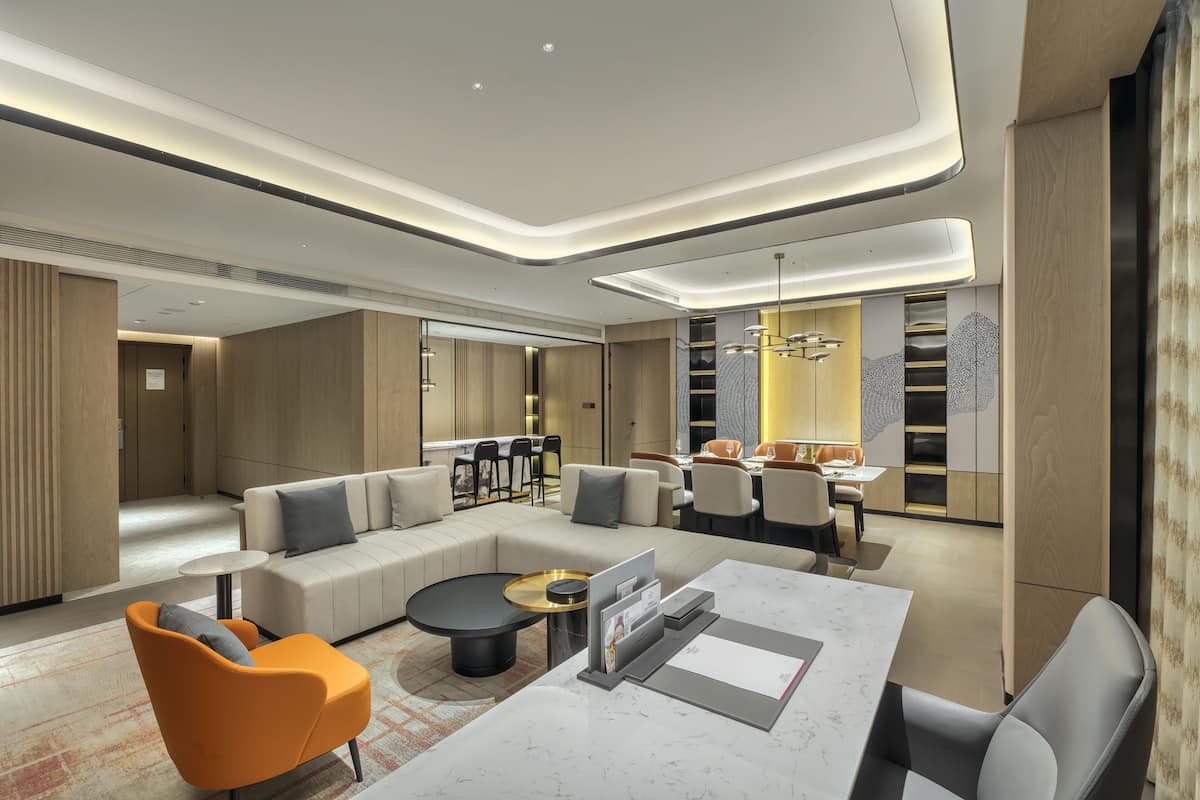 Un hall d’hôtel moderne avec un canapé d’angle, une table basse ronde et un coin repas comprenant des chaises et une table.