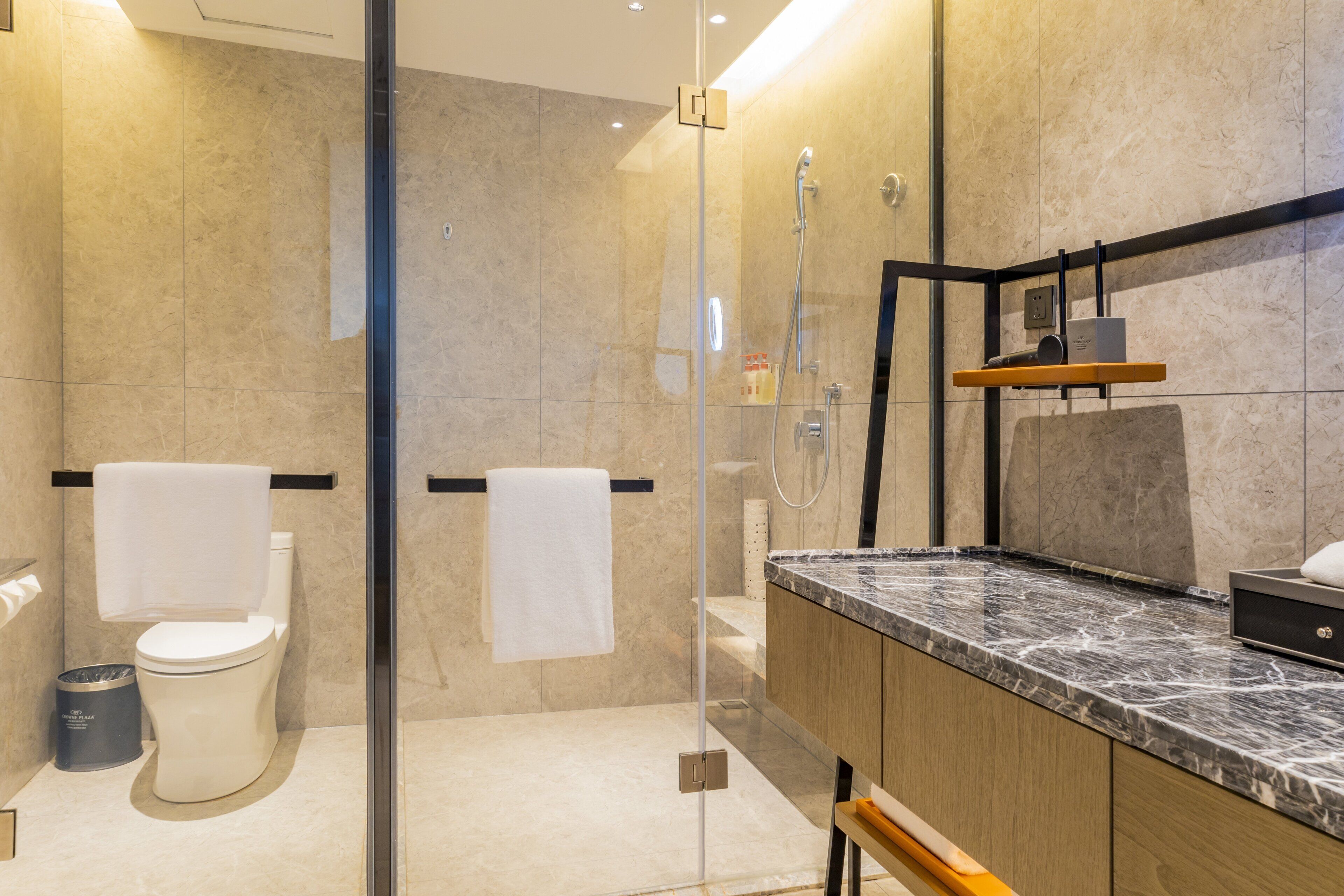 Un baño moderno con ducha de vidrio, encimera de mármol y tocador de madera.