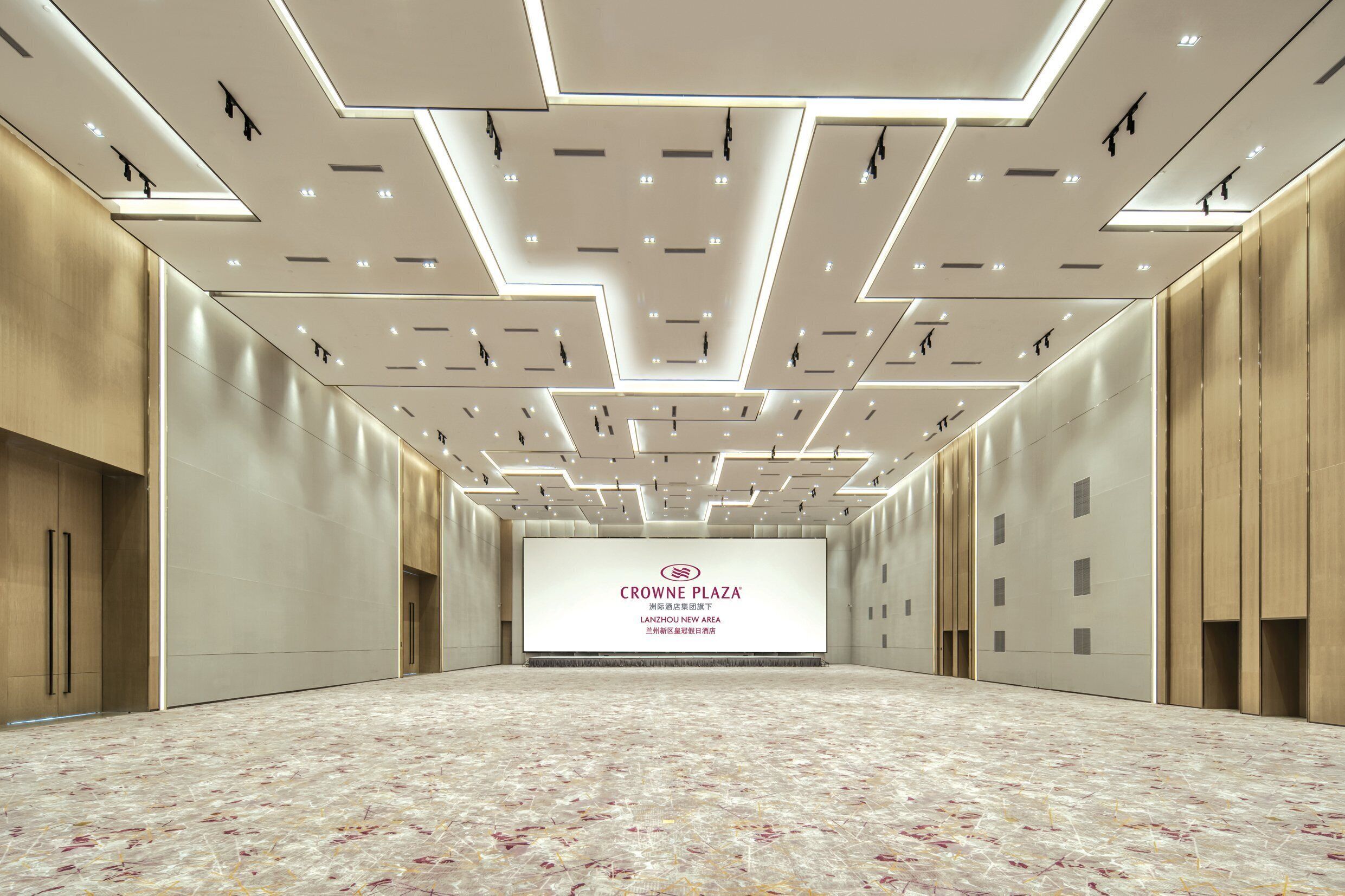 Une salle de conférence spacieuse dotée d’un plafond au design moderne, d’un grand écran affichant du texte et d’un sol à motifs.