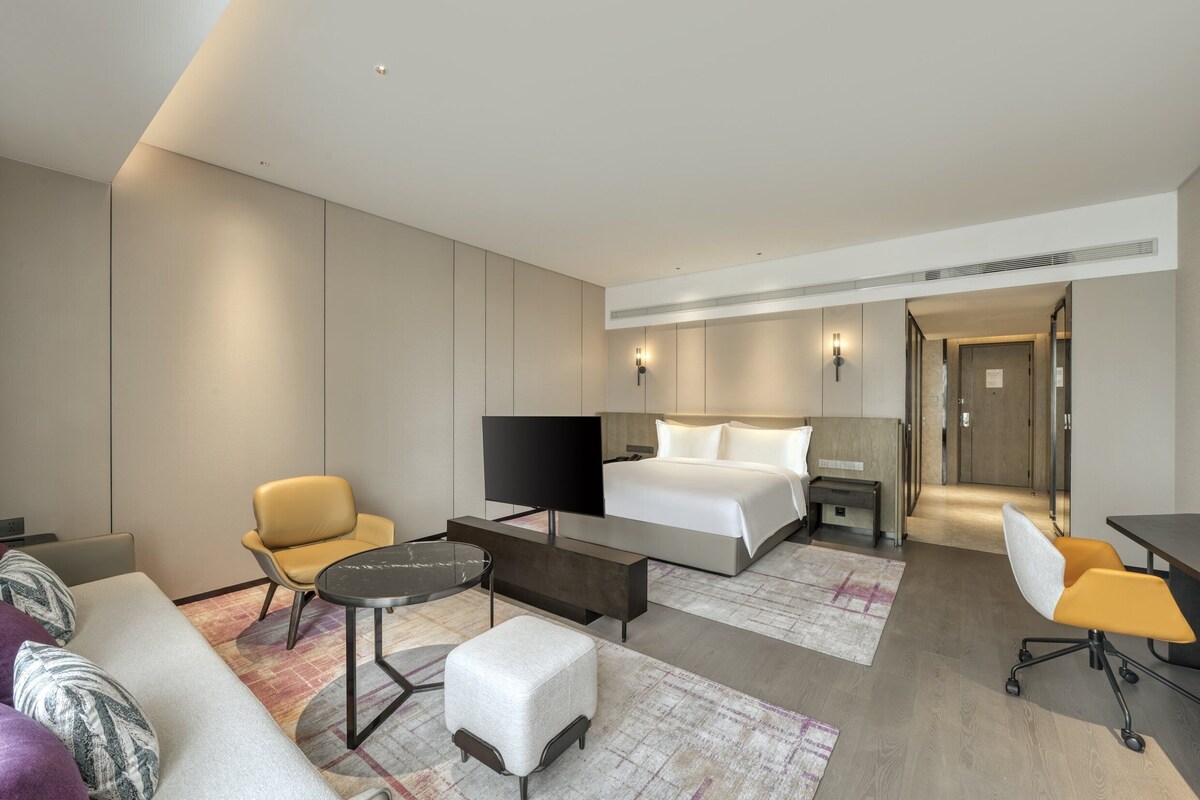Ein modernes Hotelzimmer mit Bett, Schreibtisch, Stuhl, einer Couch und einem Fernseher.