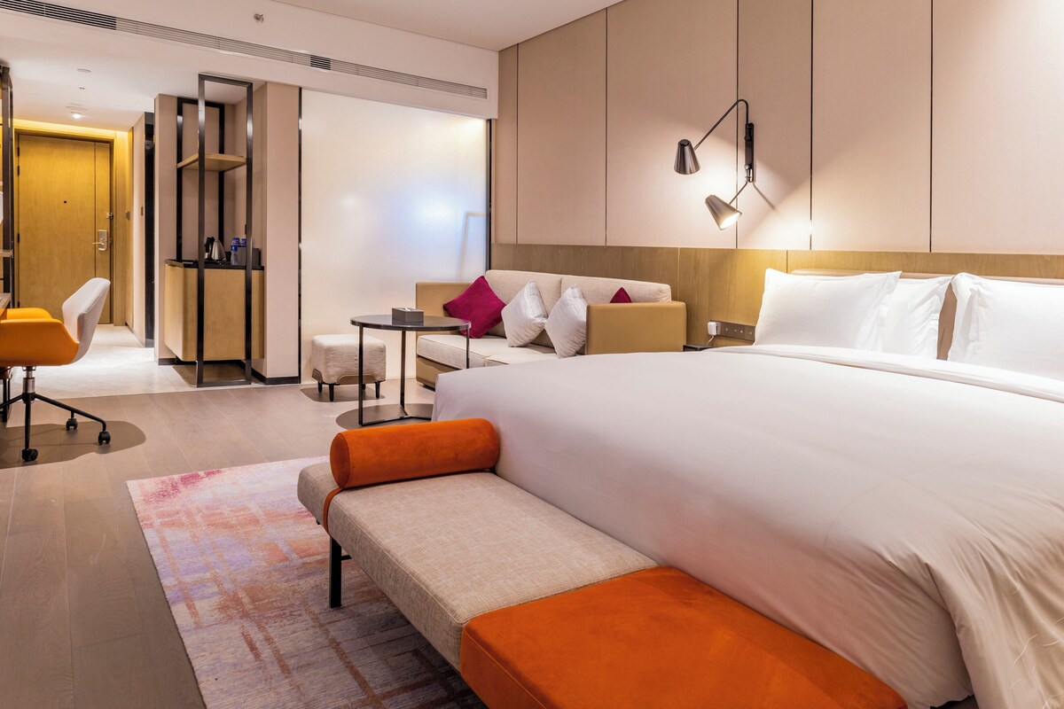Ein modernes Hotelzimmer mit einem großen Bett, einer Couch, einem Schreibtisch und einem Sessel.