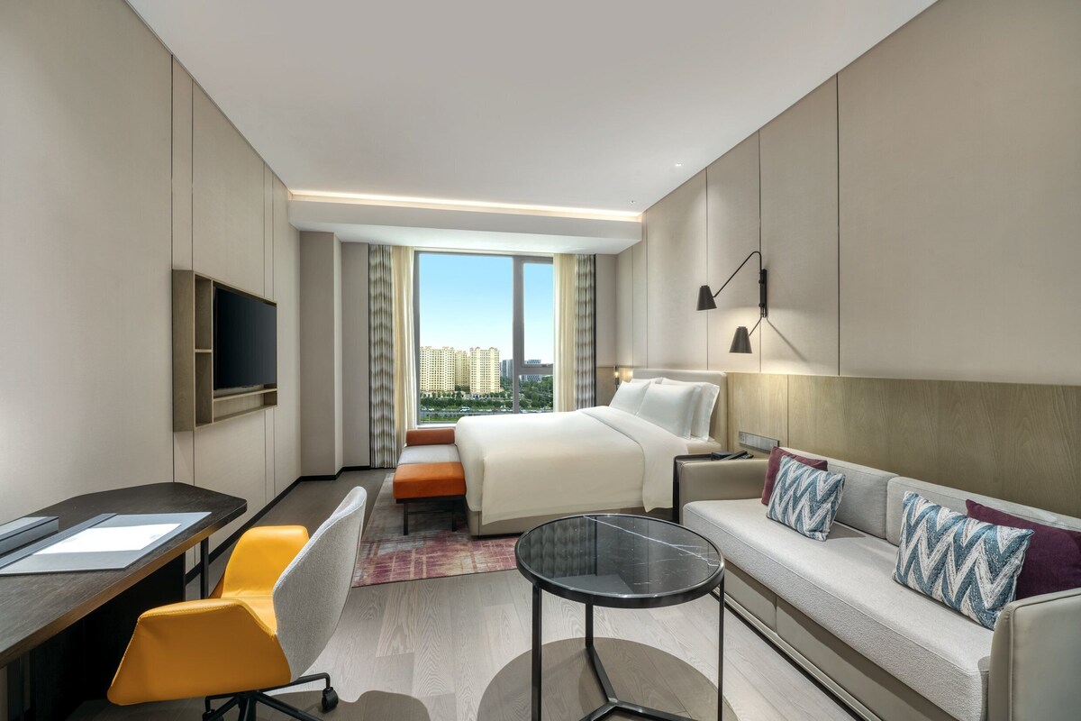 Ein modernes Hotelzimmer mit Bett, Sofa, Schreibtisch und Fernseher.