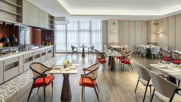 A modern restaurant with multiple dining tables and chairs, a kitchen area, and large windows allowing natural light.