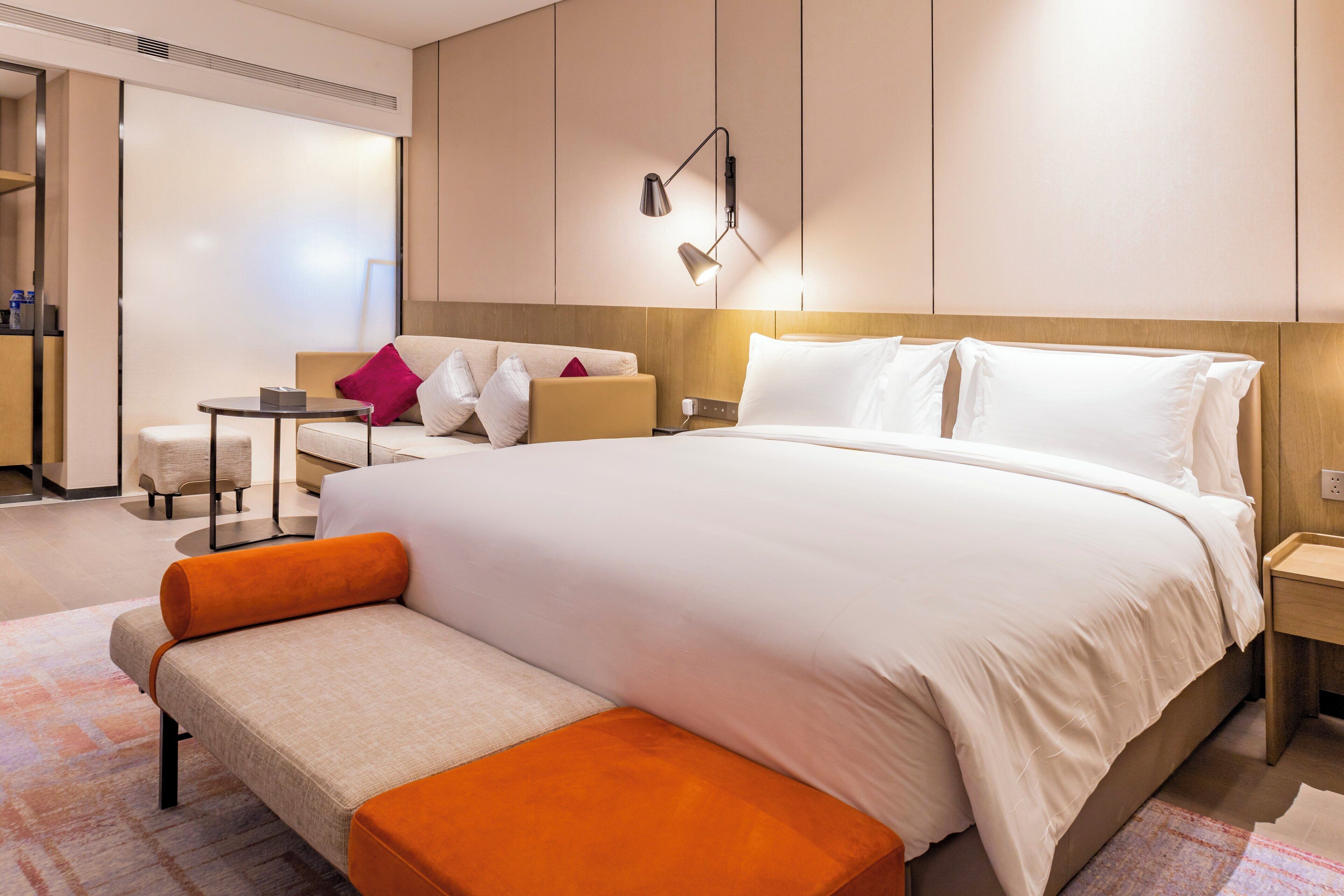 A hotel room with a large bed, a sofa, a small table, and a bench.