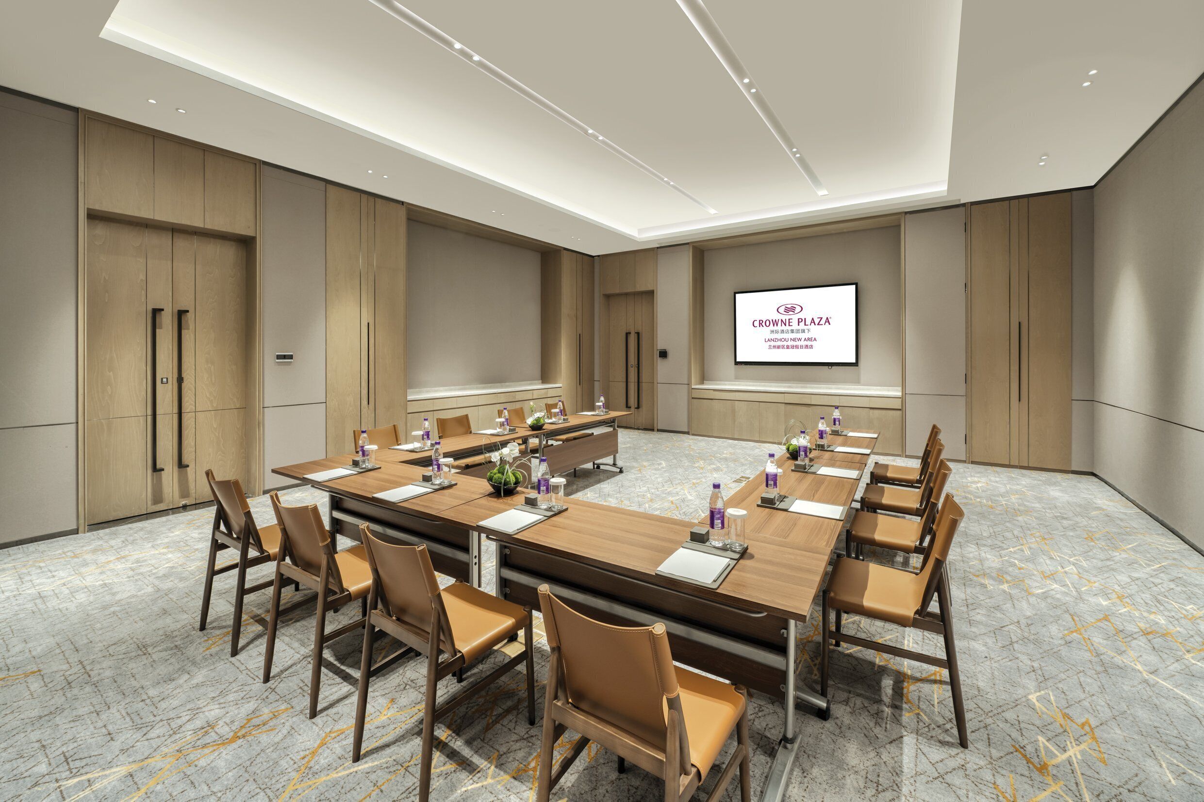Een vergaderruimte met een lange tafel, stoelen en een scherm waarop 'Crowne Plaza' staat.