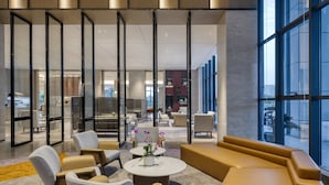 Un hall d’entrée moderne, doté d’espaces de détente, d’une table basse agrémentée de fleurs et de grandes fenêtres offrant une vue sur la ville.