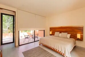 Quarto com uma cama grande, cabeceira de madeira e porta de correr de vidro que dá para um pátio externo com cadeiras.
