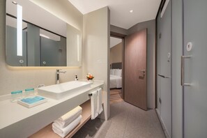 A modern bathroom with a large mirror, white sink, and a wooden door leading to a bedroom.
