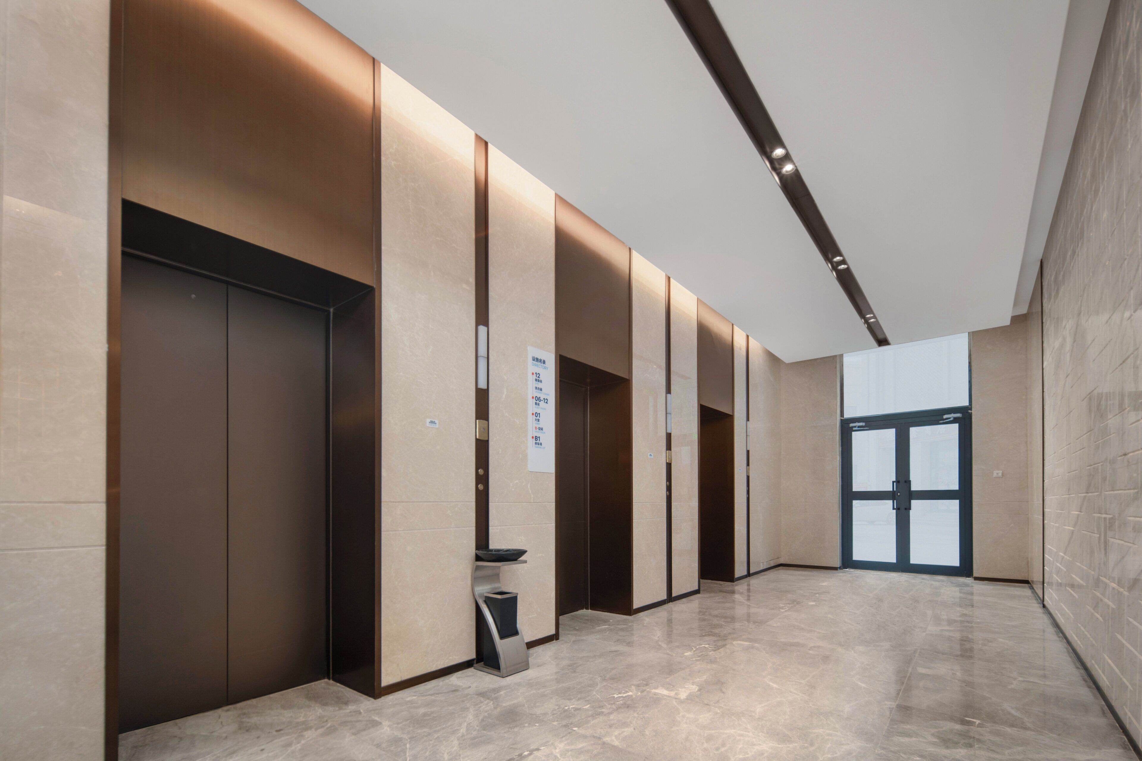 A modern elevator area with a marble floor and a glass door leading to another space.