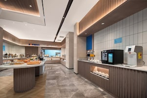 Un moderno comedor para el desayuno con una barra de buffet, una máquina de café y un dispensador de agua caliente.
