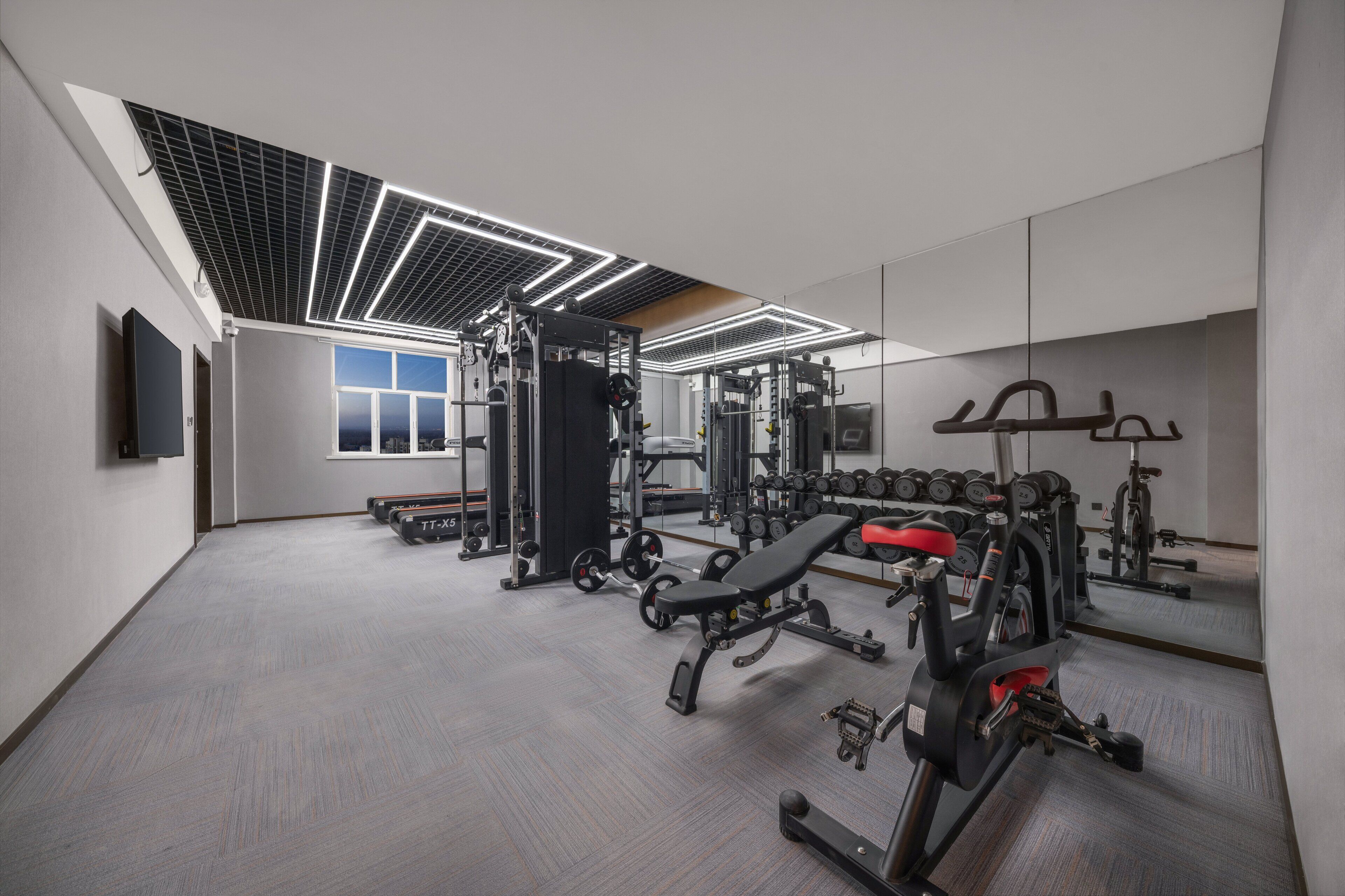 A modern gym with various exercise equipment, a bench, and a mirror on the wall.