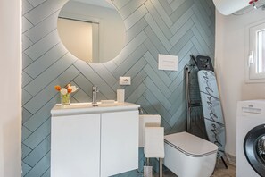 A bathroom with a herringbone tile wall, a white sink, a mirror, a towel rack, and a washing machine.