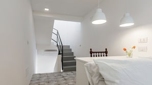Ein Schlafzimmer mit einem Bett, einem Nachttisch, einer Vase mit Blumen und einer Treppe, die in einen anderen Raum führt.