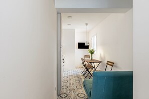 Un couloir étroit mène à un espace repas comprenant une table et des chaises, un canapé bleu et des carreaux de sol à motifs.