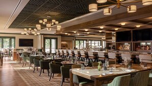 A restaurant with multiple dining tables, chairs, and a bar area with shelves of bottles.