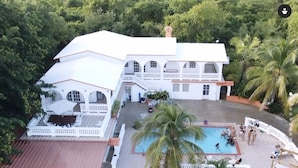 A large house with a swimming pool surrounded by palm trees and a deck area with lounge chairs. - Hacienda Victoria (Vieques)